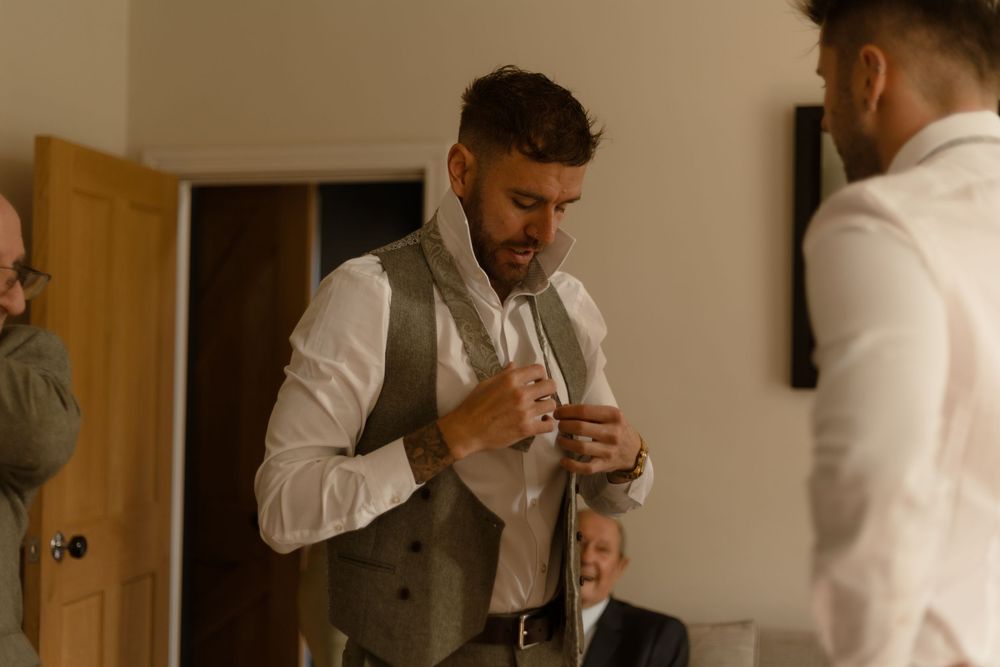 Someone in a grey vest and white shirt adjusts their tie while getting ready for a formal event.