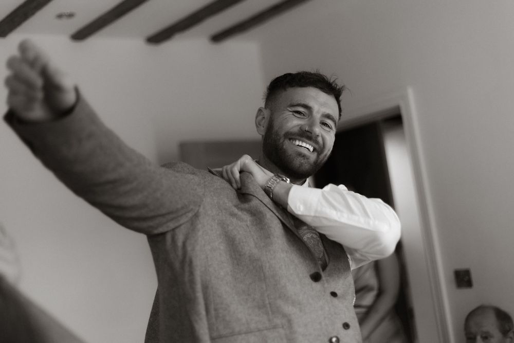 Three black and white photos show a person in a gray sweater expressing joyful emotions and gestures against a white wall.