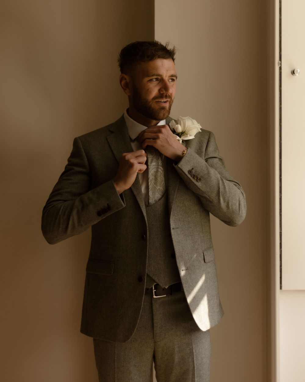 Man in a gray suit leans against a beige wall while striking dynamic poses in natural light.
