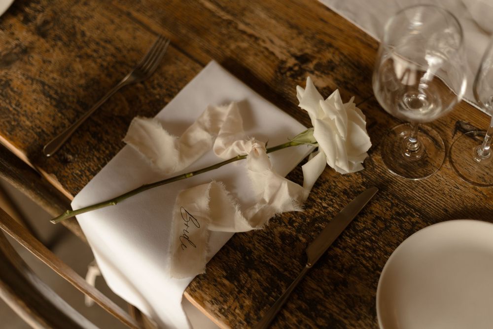 White napkin artfully folded on rustic wooden table with wine glass and place setting in warm lighting.