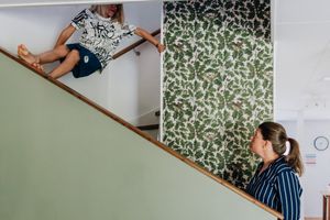 Mamman i botten av trappen pratar med barnet som är i mitten av trappen.