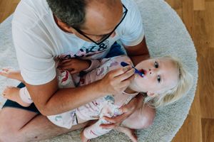 Pappan borstar tänderna på det lilla barnet i famnen.