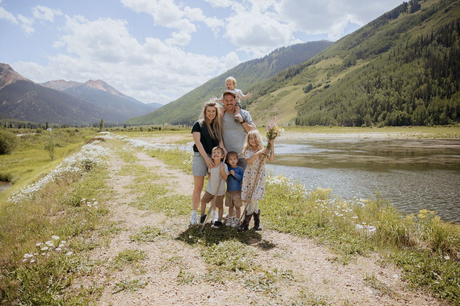Children play and explore together in a mountain meadow with scenic peaks in the background.