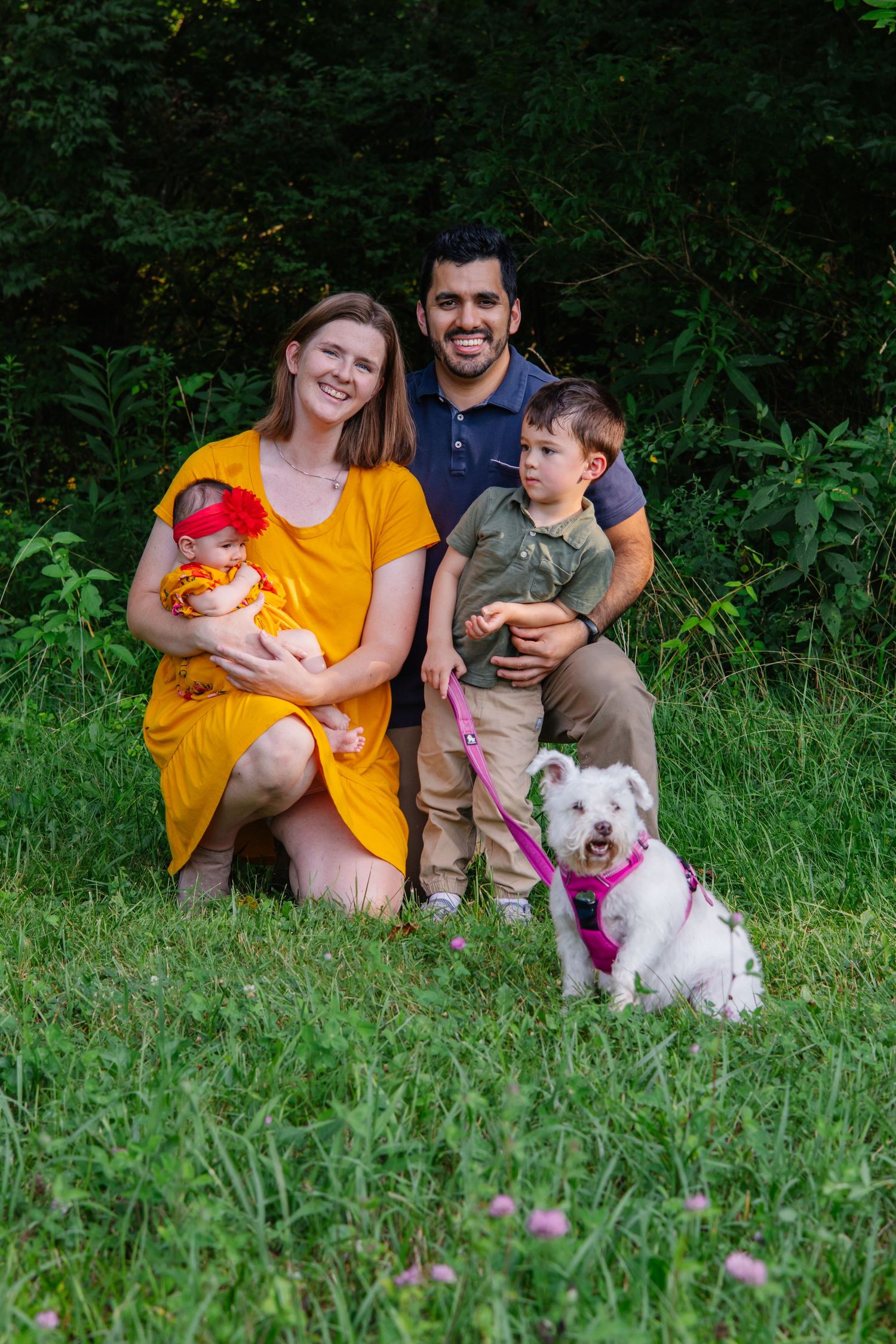 Family and their white dog sit together on grass during outdoor photo session.