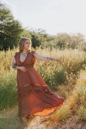 A flowing rust-colored dress twirls in golden light among desert vegetation.