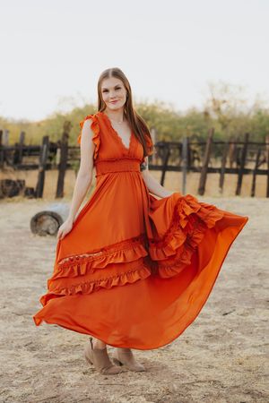 An orange ruffled dress twirls in a desert setting with wooden fence posts in the background.