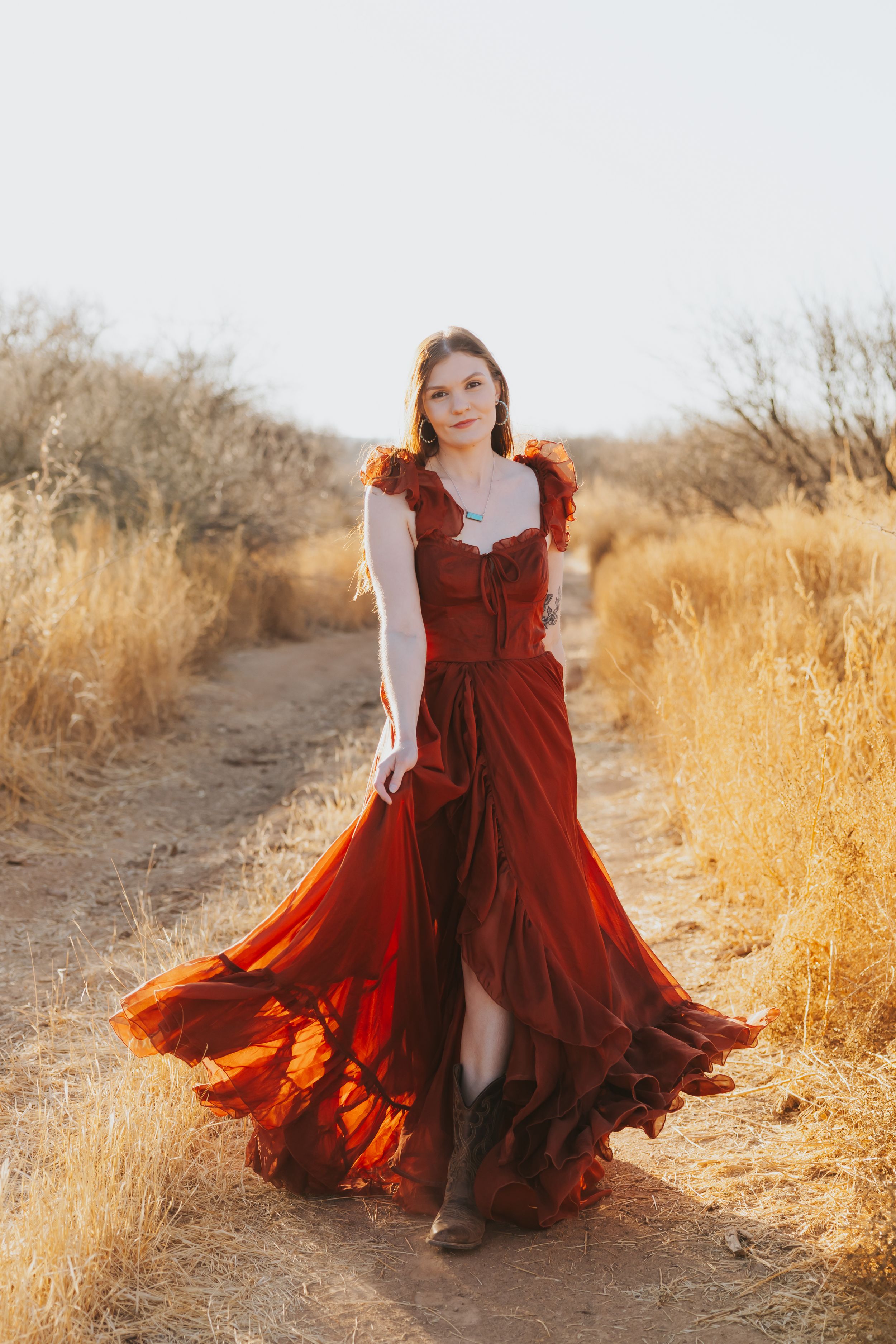 A burgundy dress flows dramatically along a desert path during golden hour.