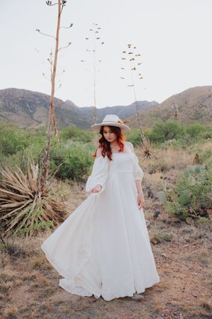 A flowing white dress twirls against a desert mountain backdrop with saguaro cacti and desert vegetation.