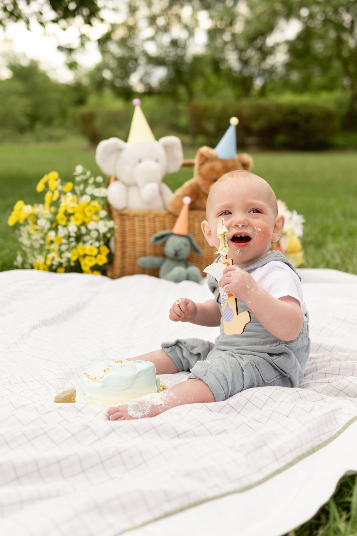 A springtime picnic setup outdoors with stuffed animals and party hats on for a cake smash by Haddonfield family and milestone photographer