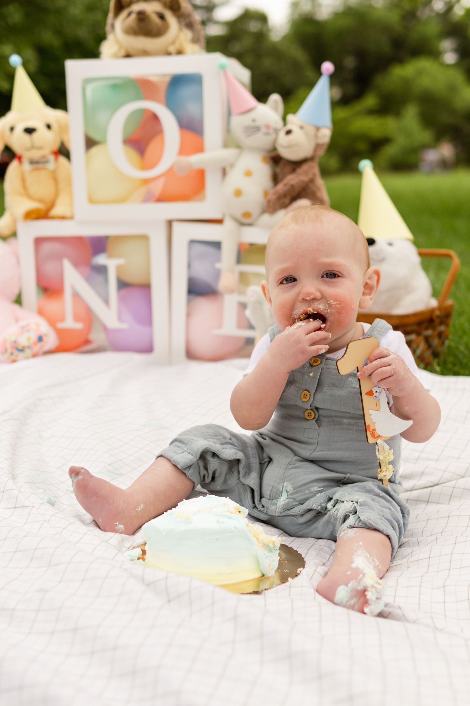 Baby boy eats cake as he celebrates his first birthday with a cake smash at a park in South Jersey, NJ
