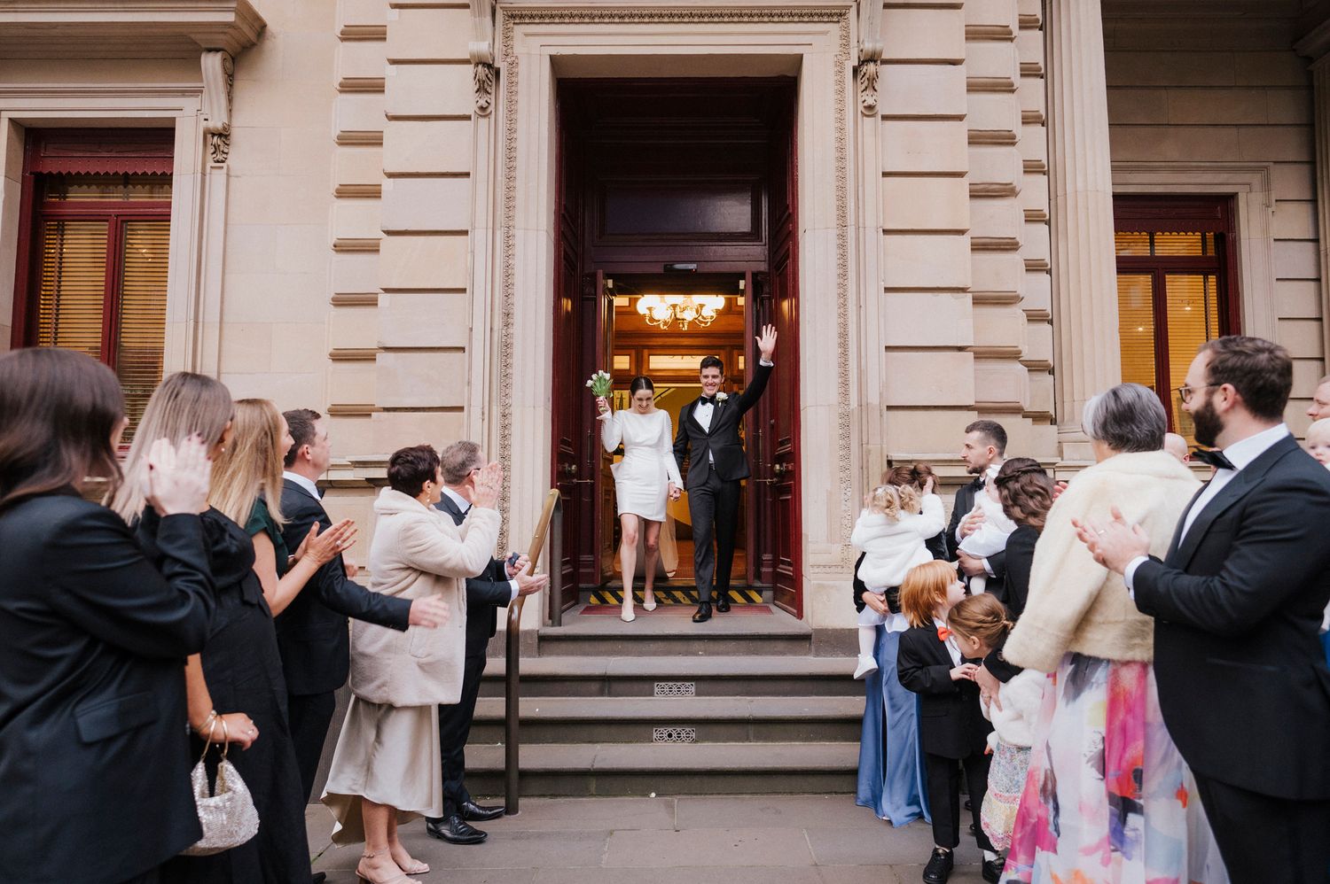 Wedding celebration outside a classical building with arched architecture.