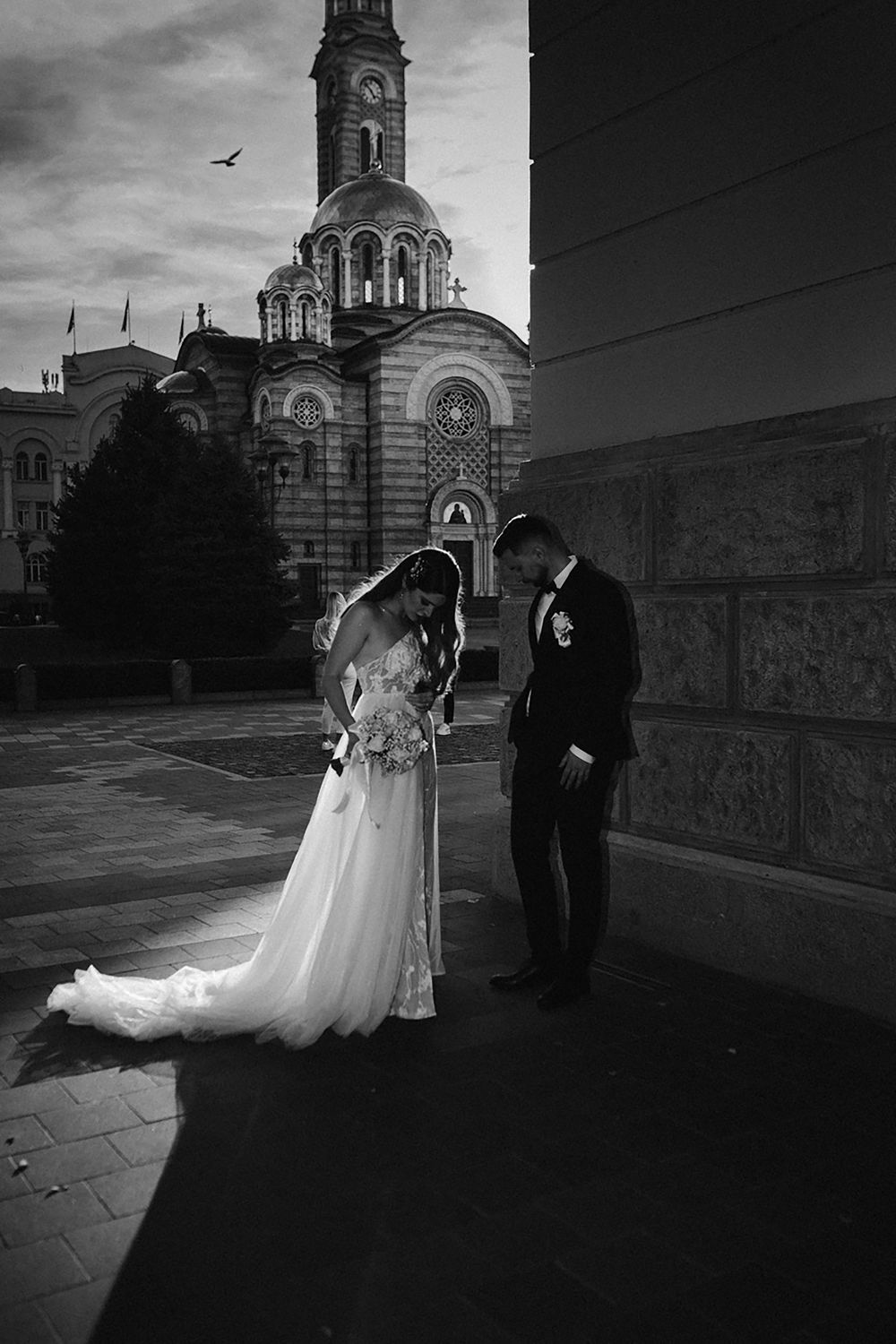 A black and white church wedding series showcases a couple by ornate stone architecture at dusk, their silhouettes striking.