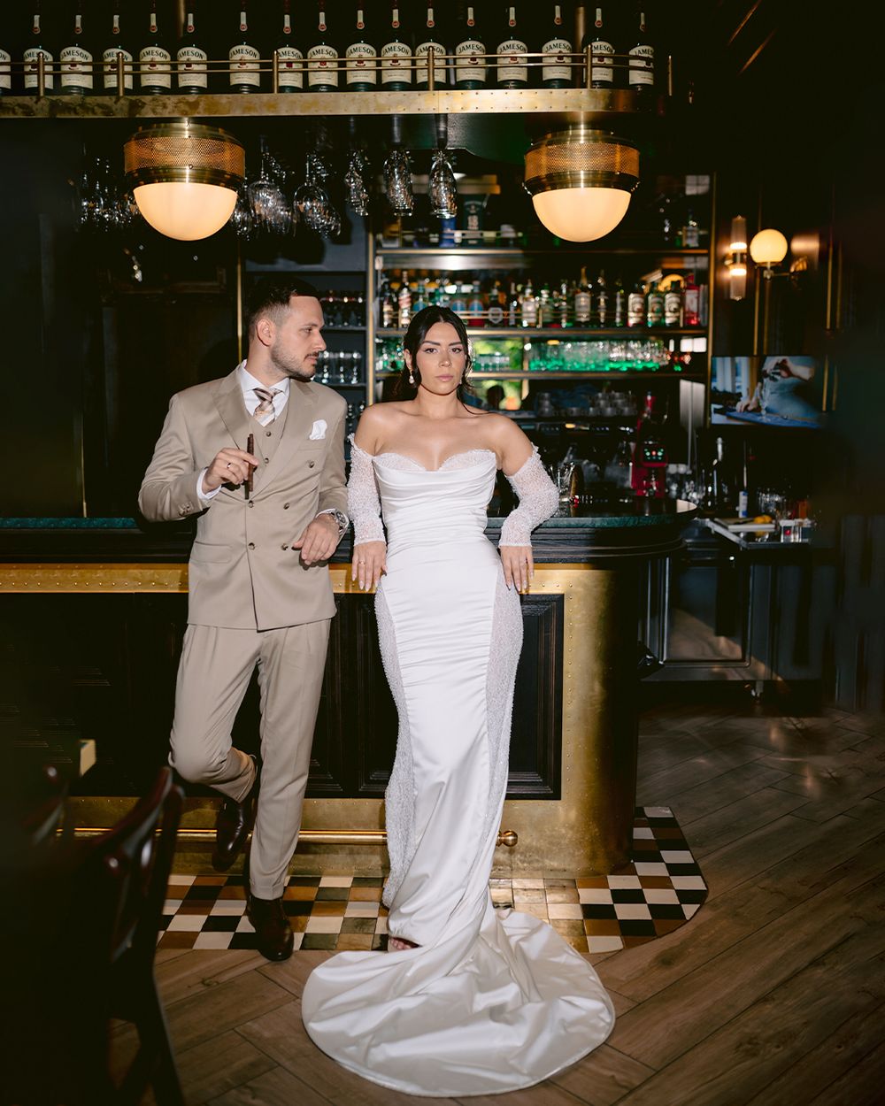 A couple in wedding attire shares an intimate dance moment at a retro-styled venue with checkerboard floors and vintage lighting.