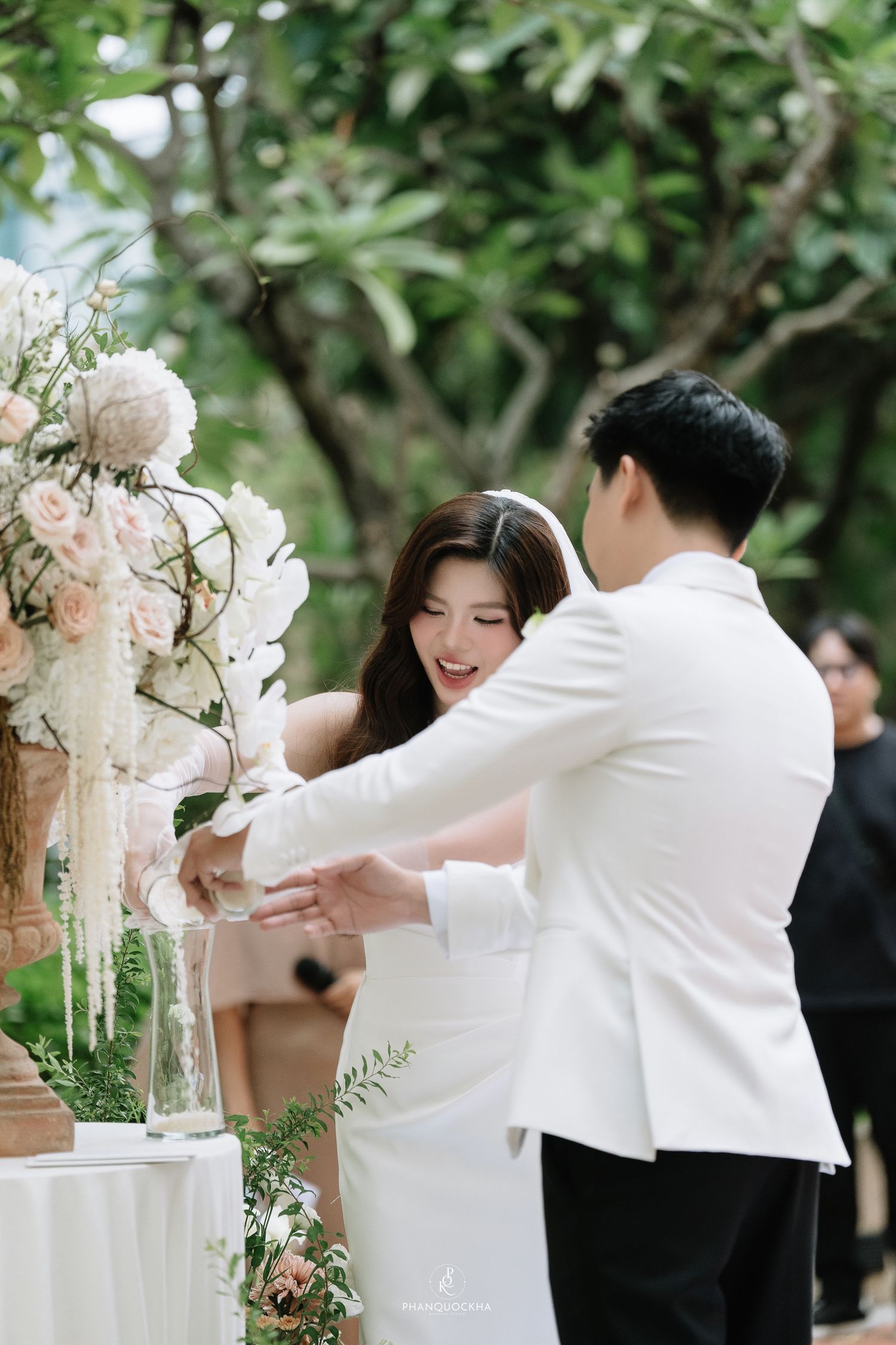 Bride and groom laugh together while performing a unity ceremony at their outdoor wedding.