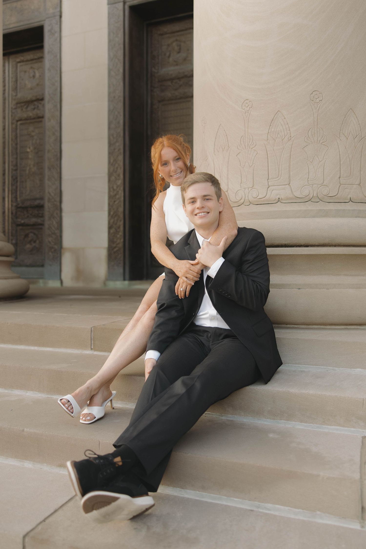A couple in formal attire sitting on stone steps together during an outdoor photoshoot.