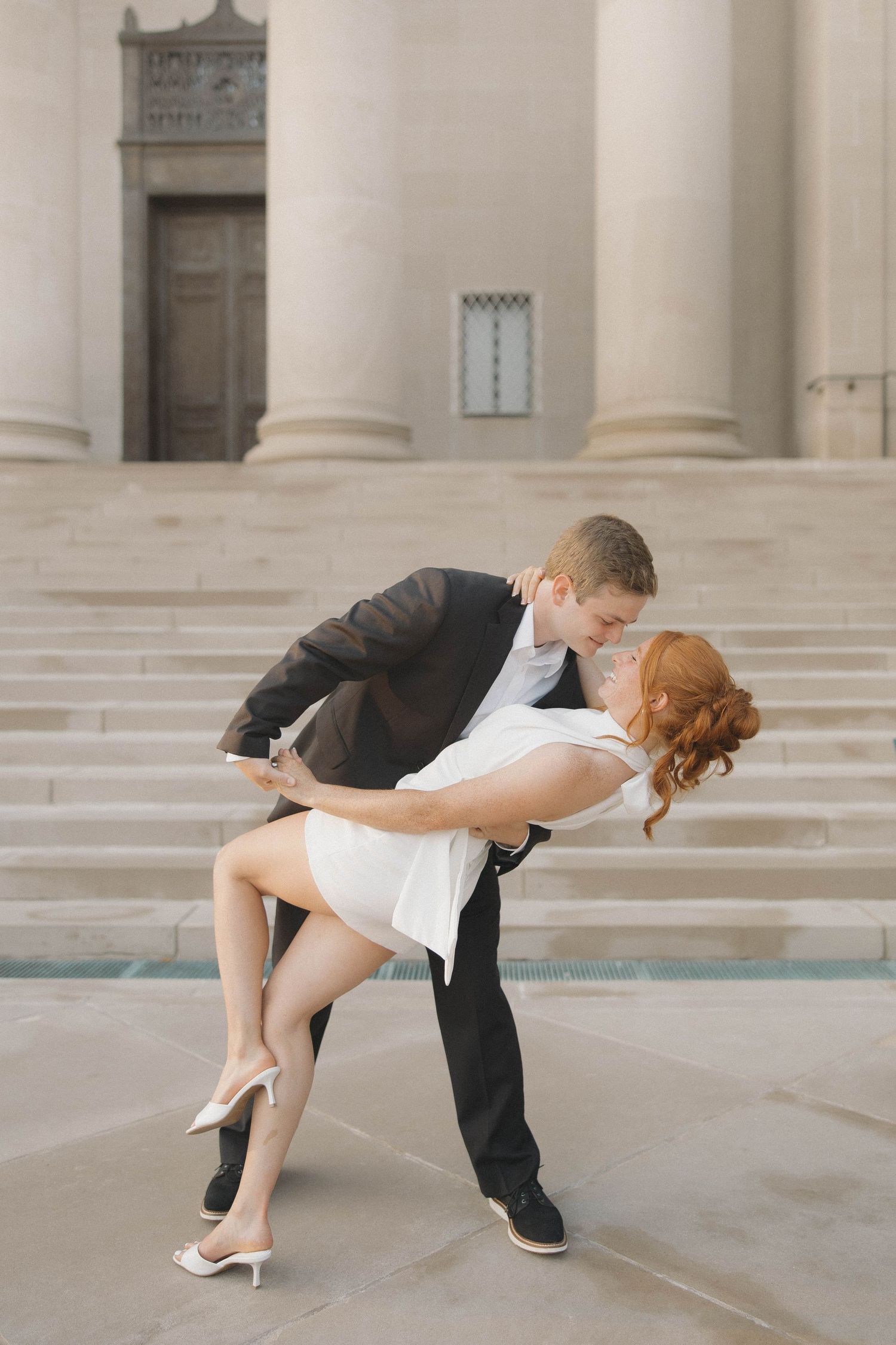 A couple performs a dramatic dance dip pose in front of classical stone columns and pillars.
