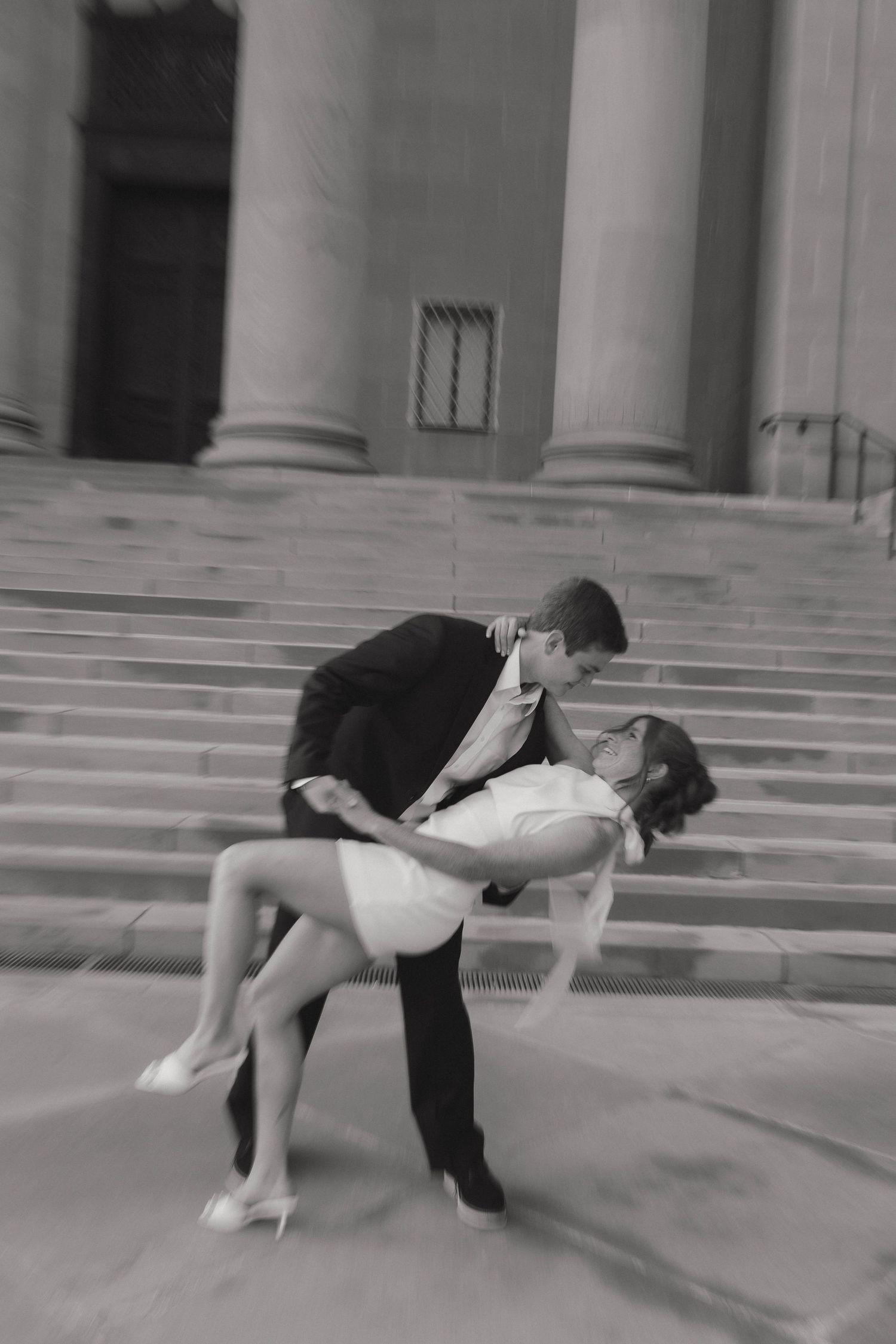 A romantic black and white photo of a couple dancing on stone steps, with the man dipping his partner in an elegant pose.