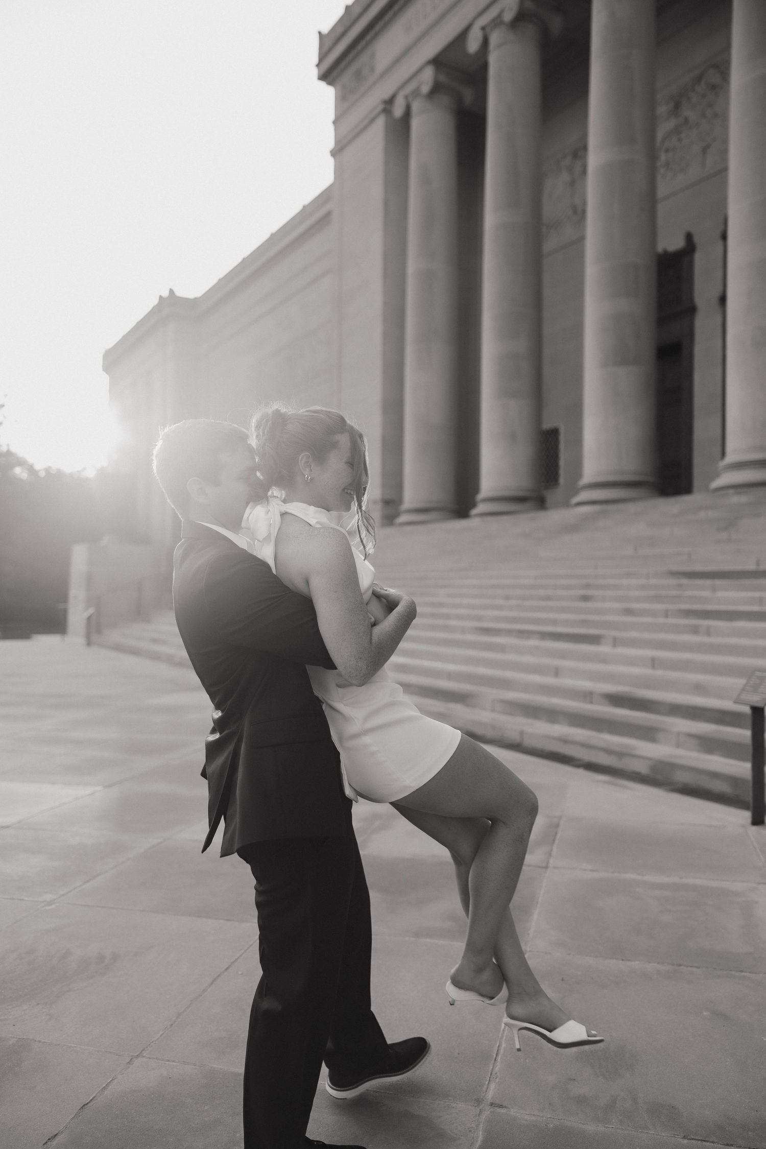 A romantic dance sequence shown in a black and white photo series on steps of a classical building with sunlight flare.