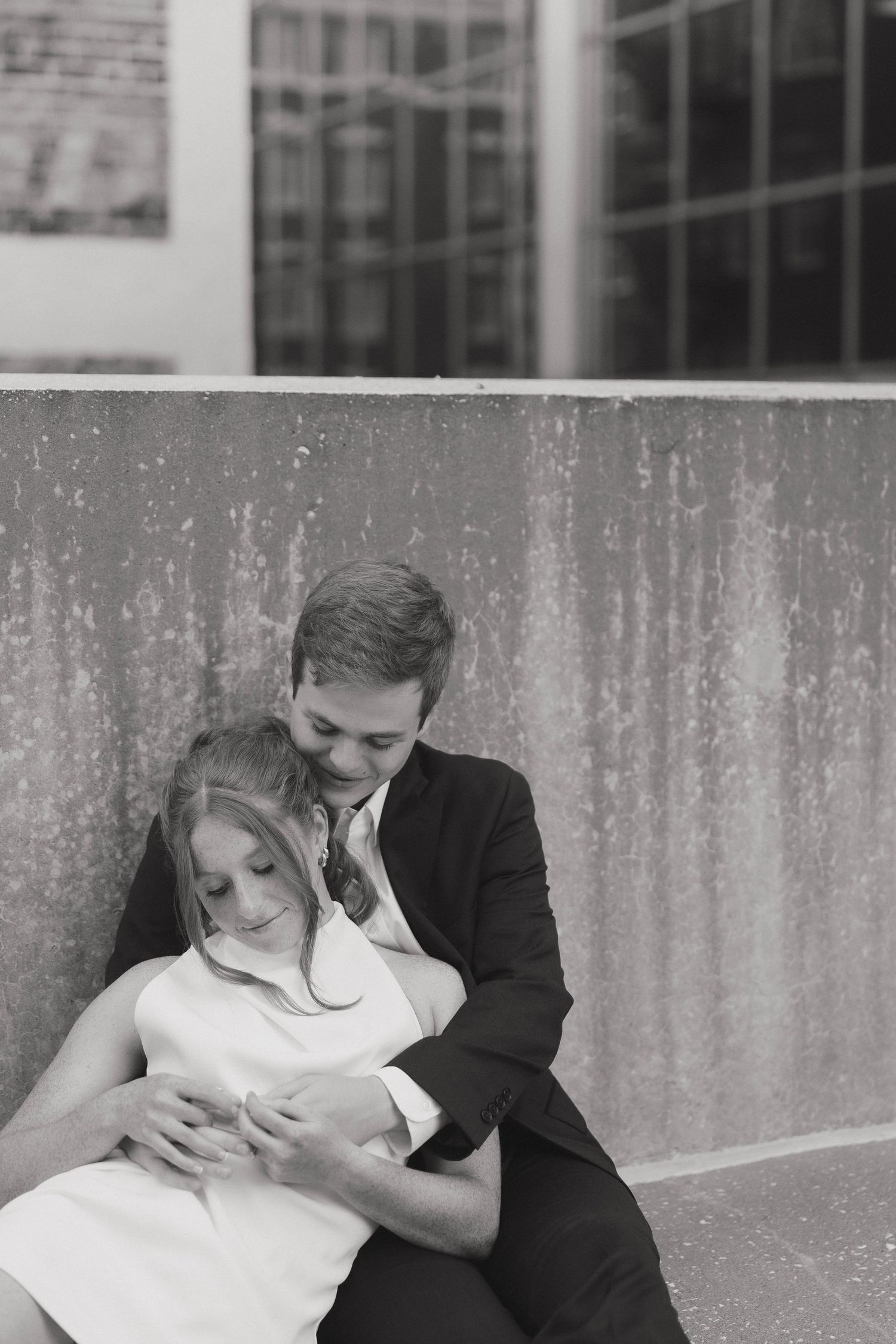 Two elegantly dressed dancers move gracefully together against a concrete wall with a fountain feature.