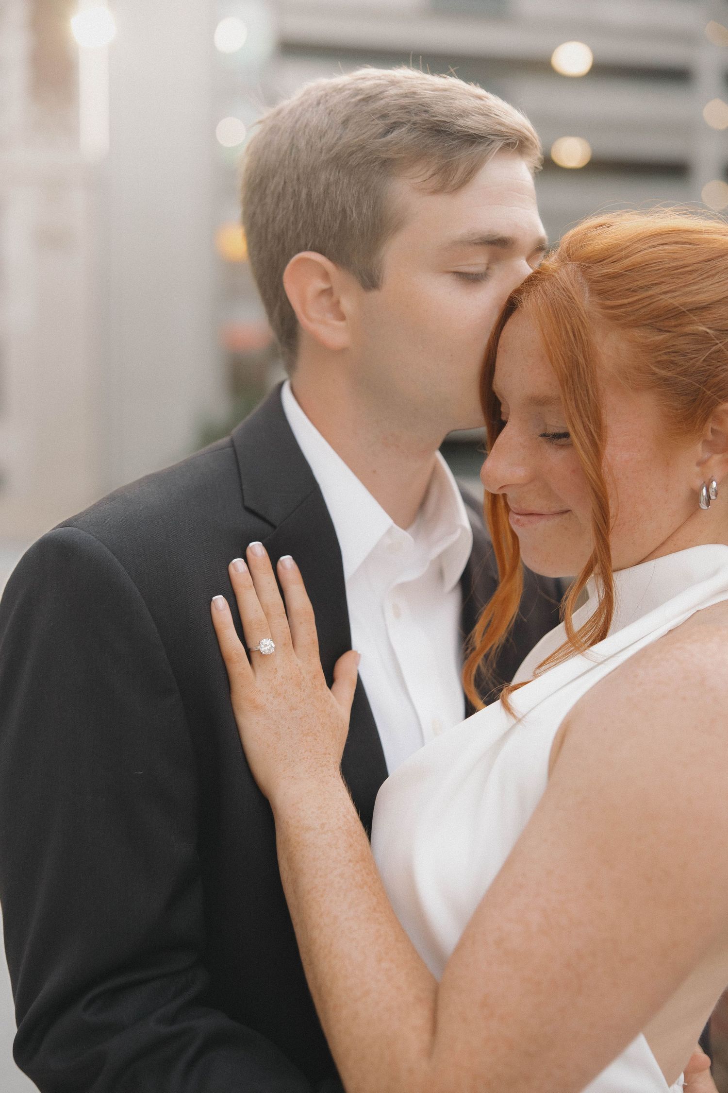 Intimate moment between a couple in formal attire with soft lighting and urban backdrop.