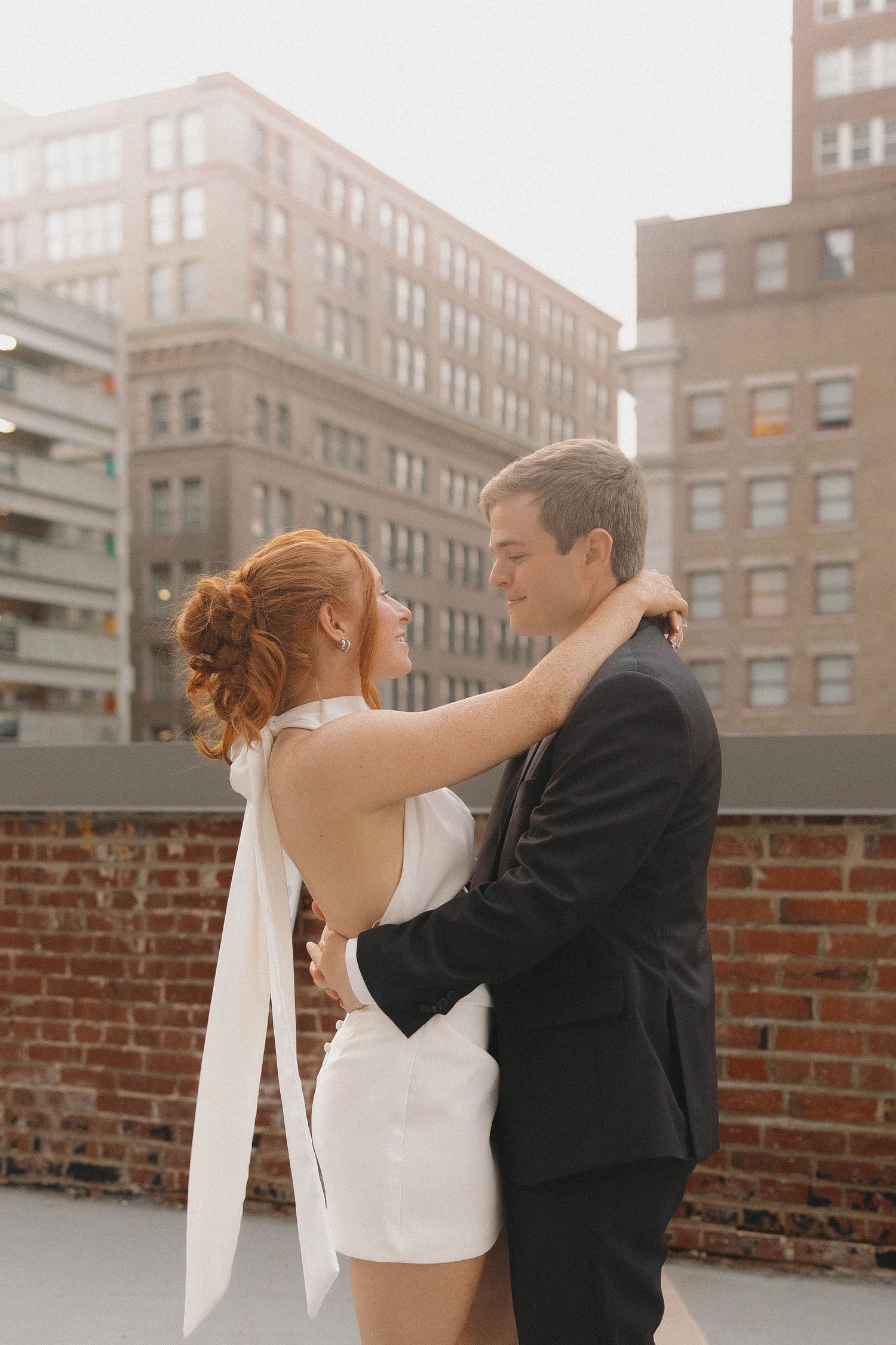 A couple embraces on a rooftop with urban buildings in the background during a wedding photoshoot.