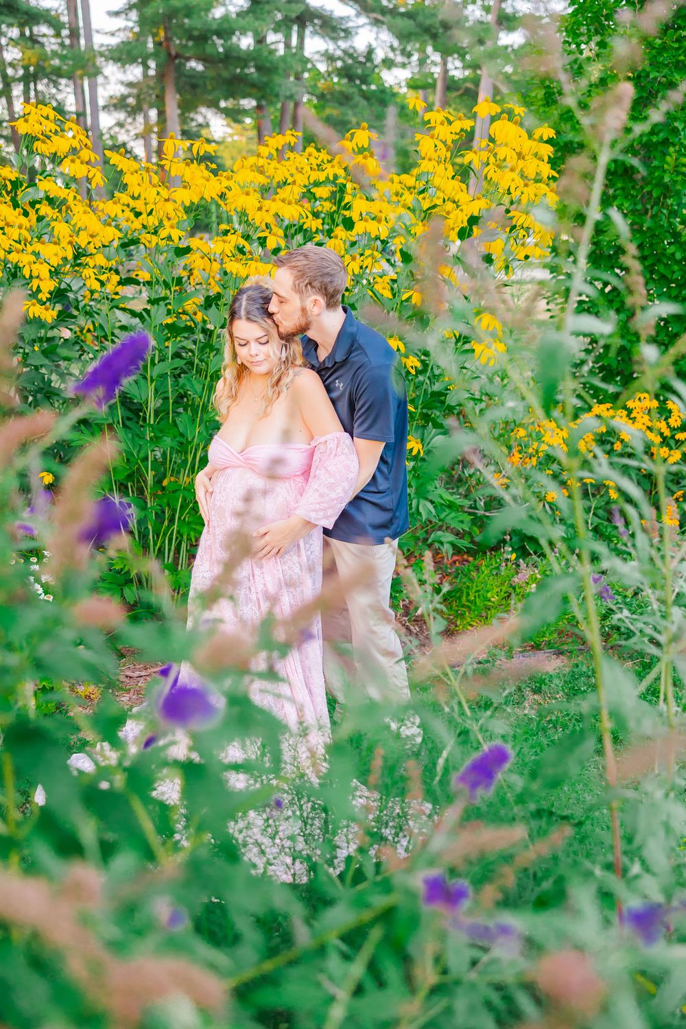 A romantic couple shares tender moments among blooming yellow wildflowers and purple flowers in a lush garden setting.
