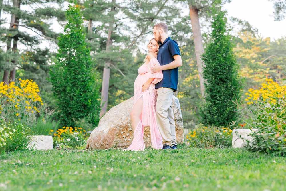 A couple shares a romantic moment surrounded by colorful gardens and evergreen trees on a sunny day.