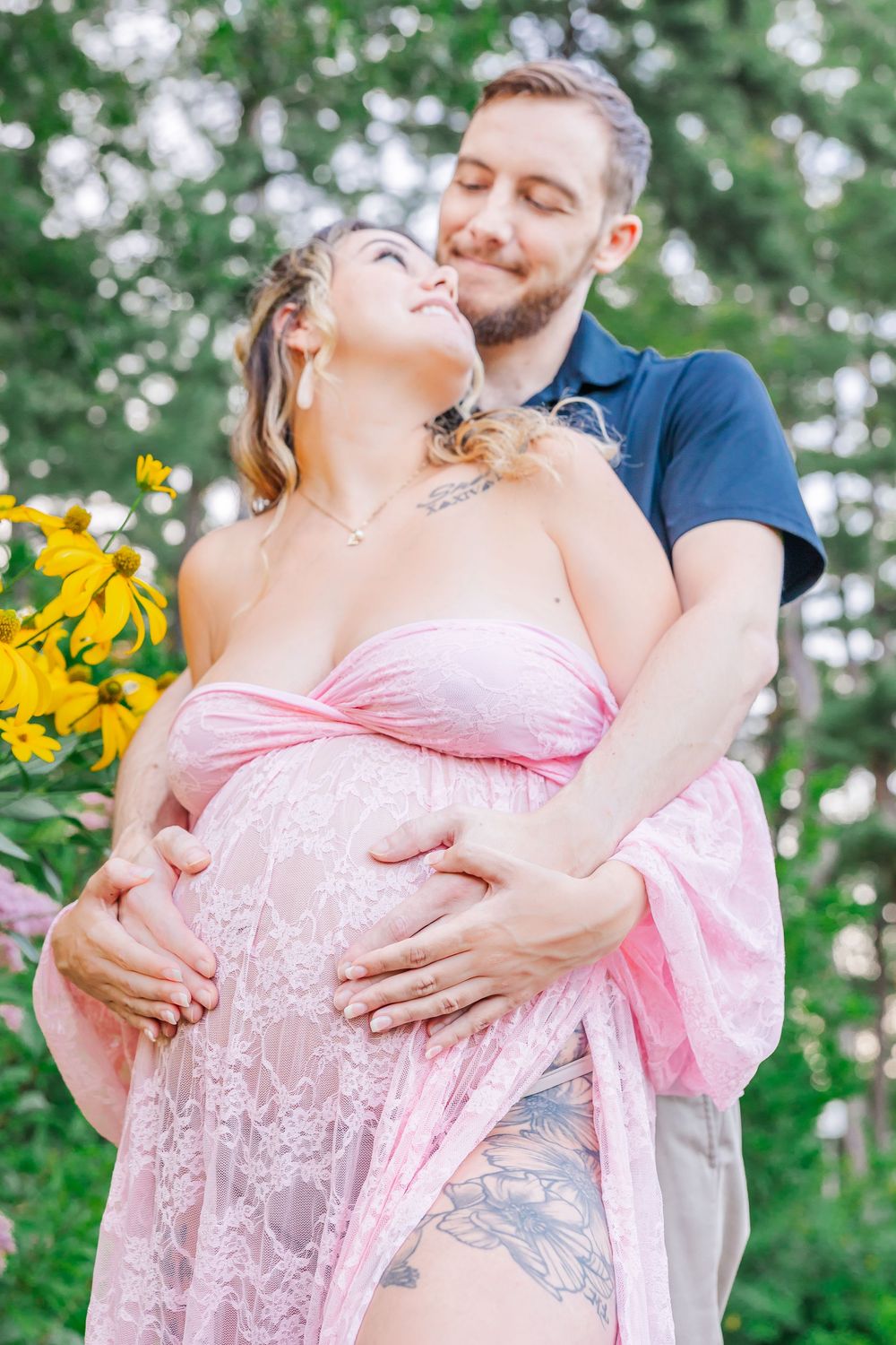 A romantic maternity photo shoot in nature featuring a couple embracing among yellow flowers and greenery.