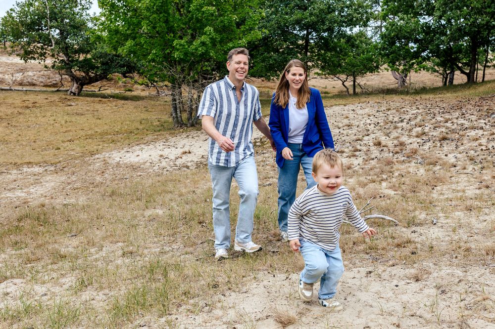 Klein jongetje loopt vrolijk vooruit met zijn ouders op de achtergrond tijdens een fotoshoot in de duinen
