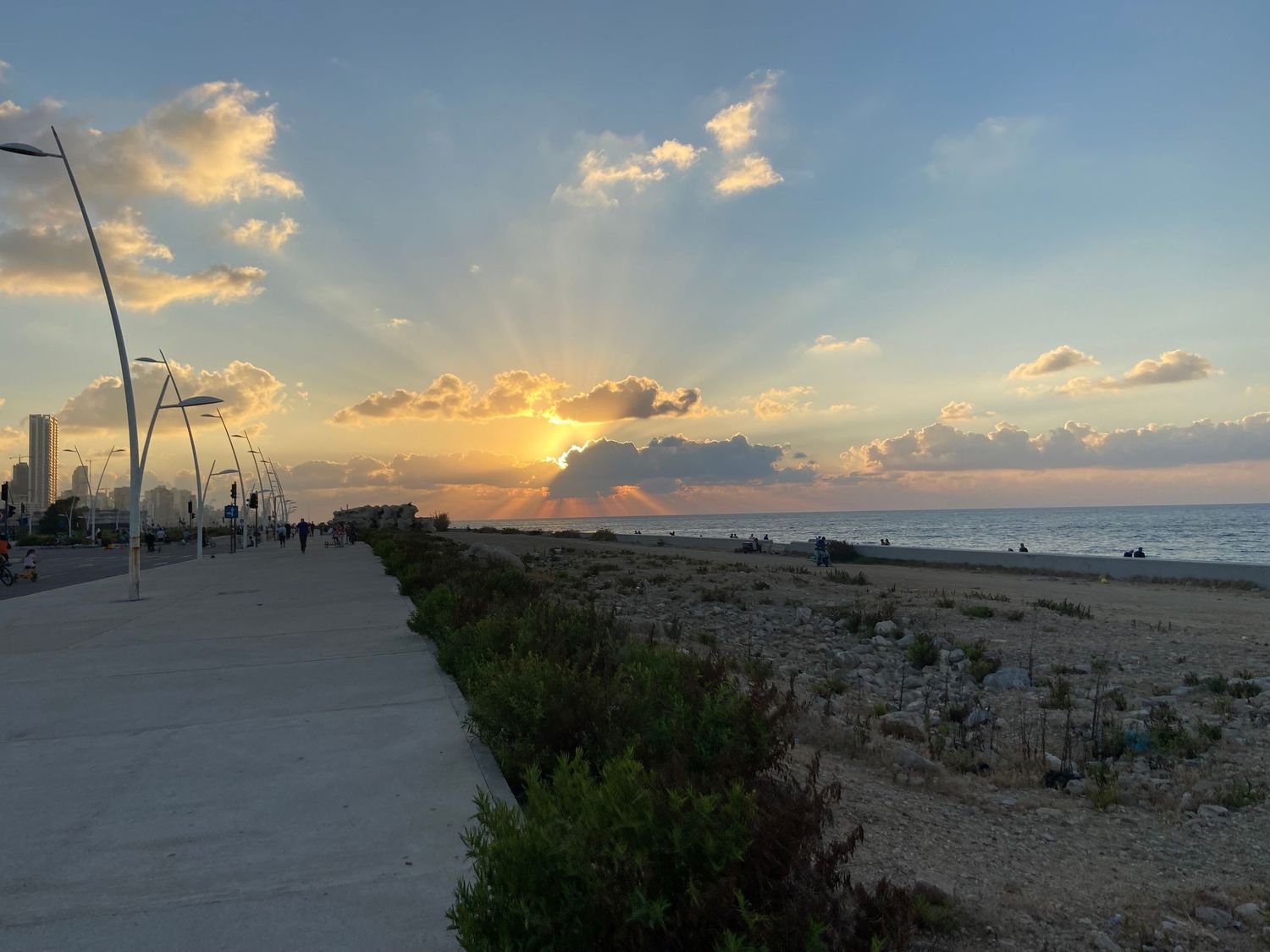 Beach boardwalk at sunset with scattered clouds and golden sunbeams over ocean horizon.