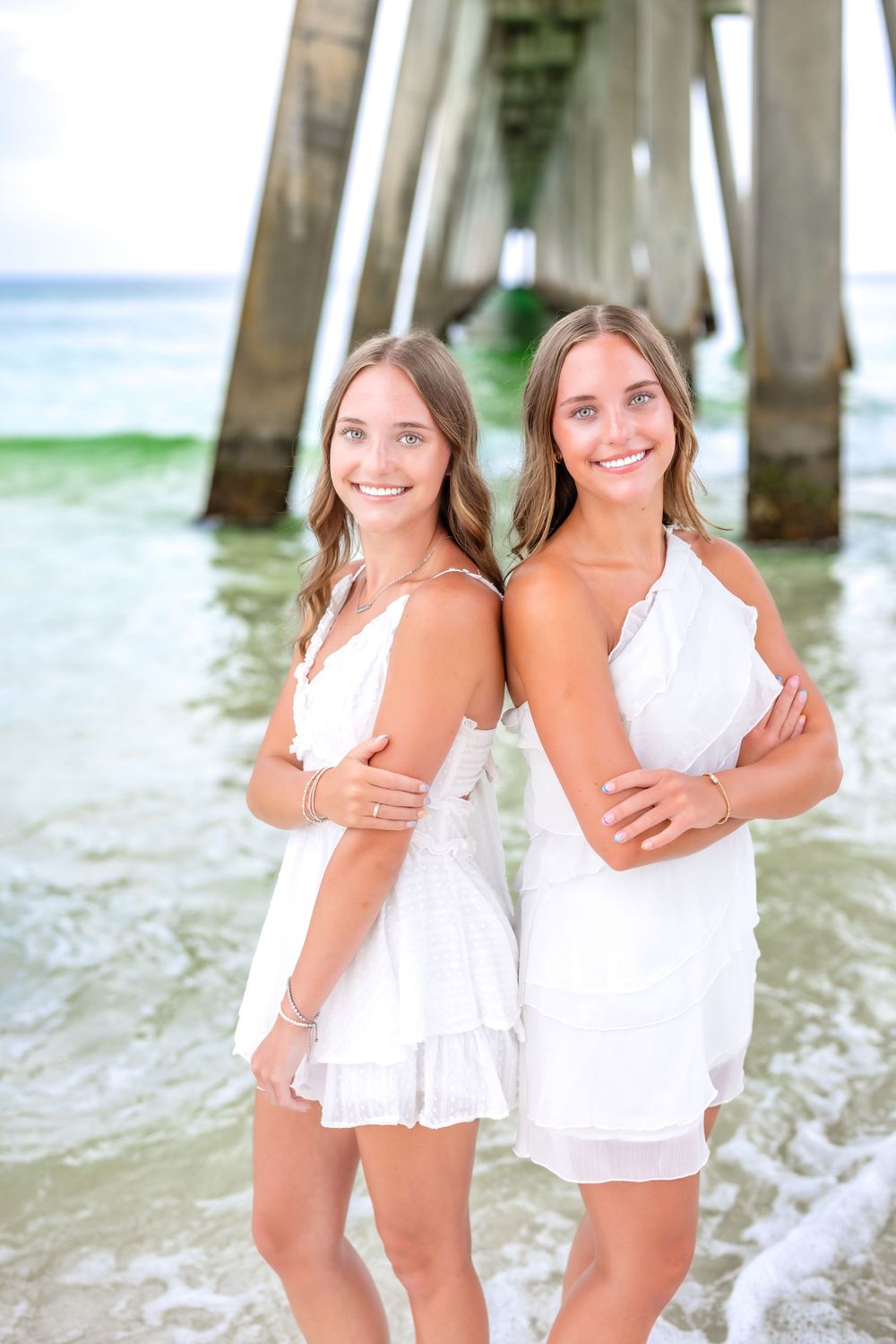 Two people in white outfits playing and laughing together on a beach near ocean waves.