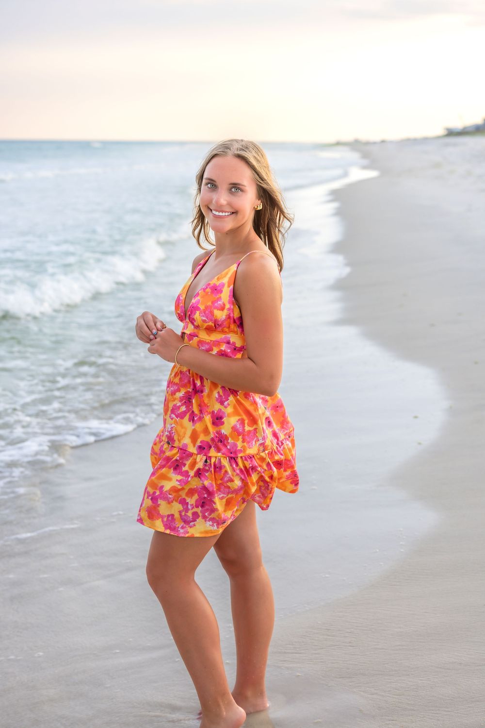 Woman in bright floral dress enjoys a carefree moment on beach at sunset.