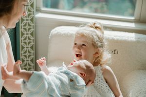 Baby laughing while lying on bed near window with natural light streaming in during daytime.