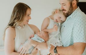 A peaceful family moment as parents hold their sleeping newborn and young child in a light-filled room.