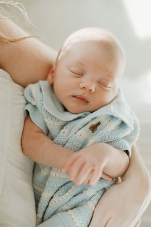 Sleeping newborn wearing light blue knit sweater rests peacefully against soft white fabric.