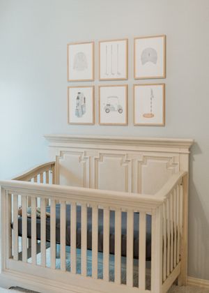 A neutral-colored nursery with a wooden crib and six framed prints featuring minimalist transportation-themed artwork.