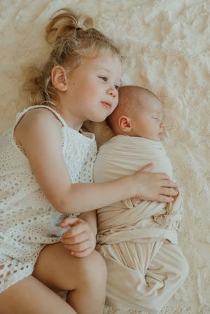 Four sequential photos showing a tender moment between siblings cuddling together on a cream-colored blanket.