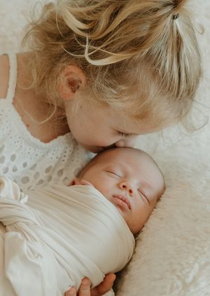 Tender moment captured of parent and newborn baby sleeping peacefully together in soft white bedding.