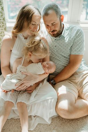 Family sharing tender moments together on a sunlit carpet by large windows.