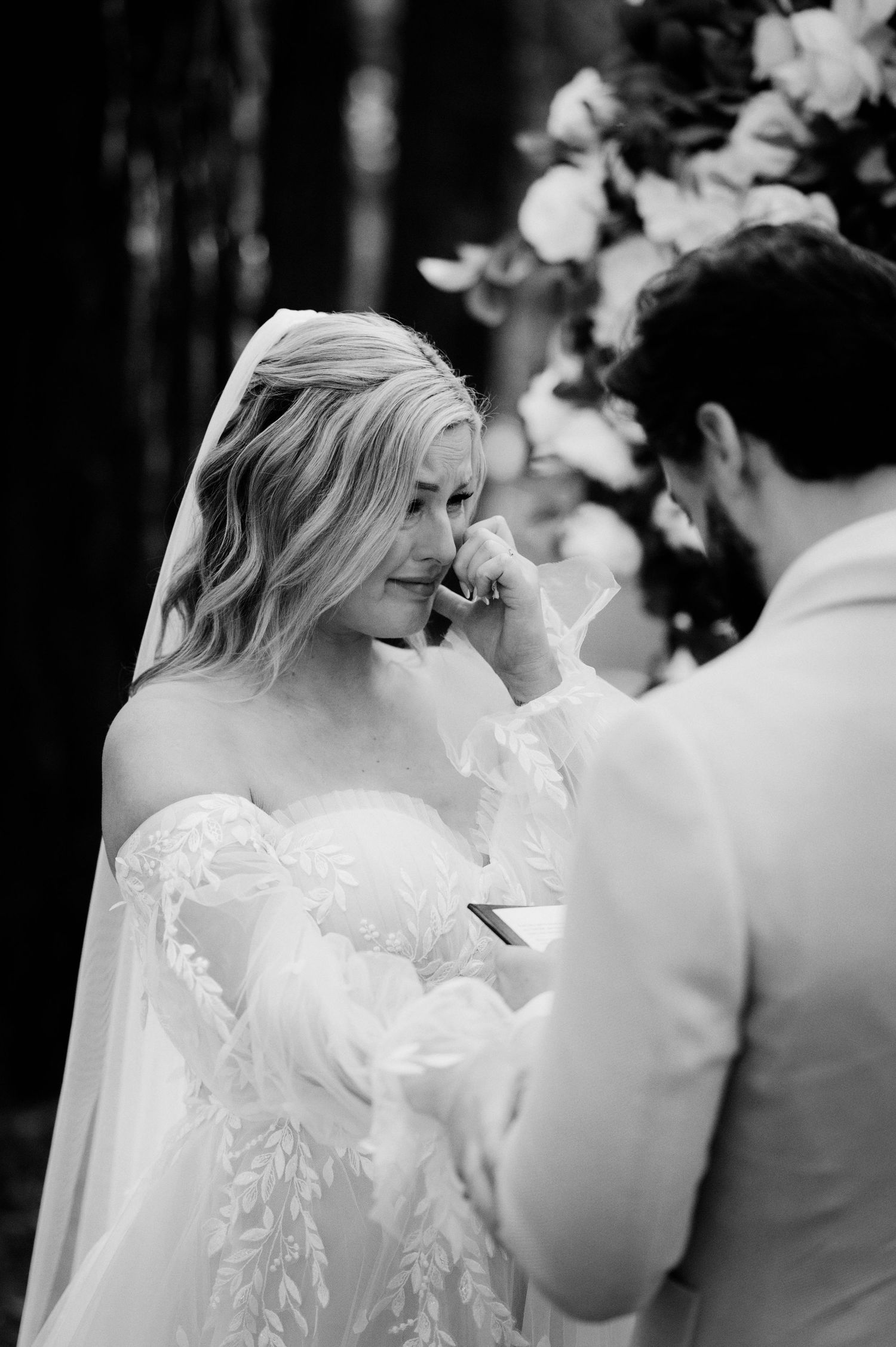A tender black and white wedding moment between newlyweds during their outdoor ceremony with floral decor.