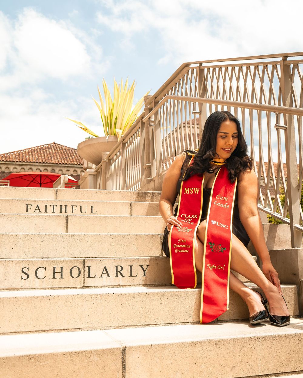 Female USC graduate wearing red MSW honor stole sitting on campus steps labeled “Faithful” and “Scholarly."
