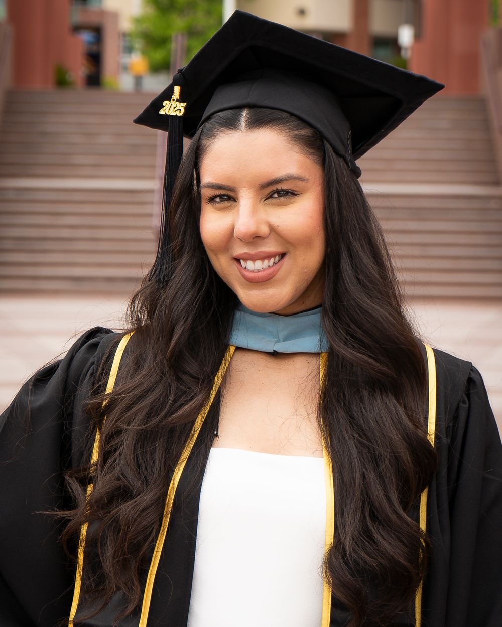 Graduate in cap and stole poses beside a California State University Los Angeles sign.