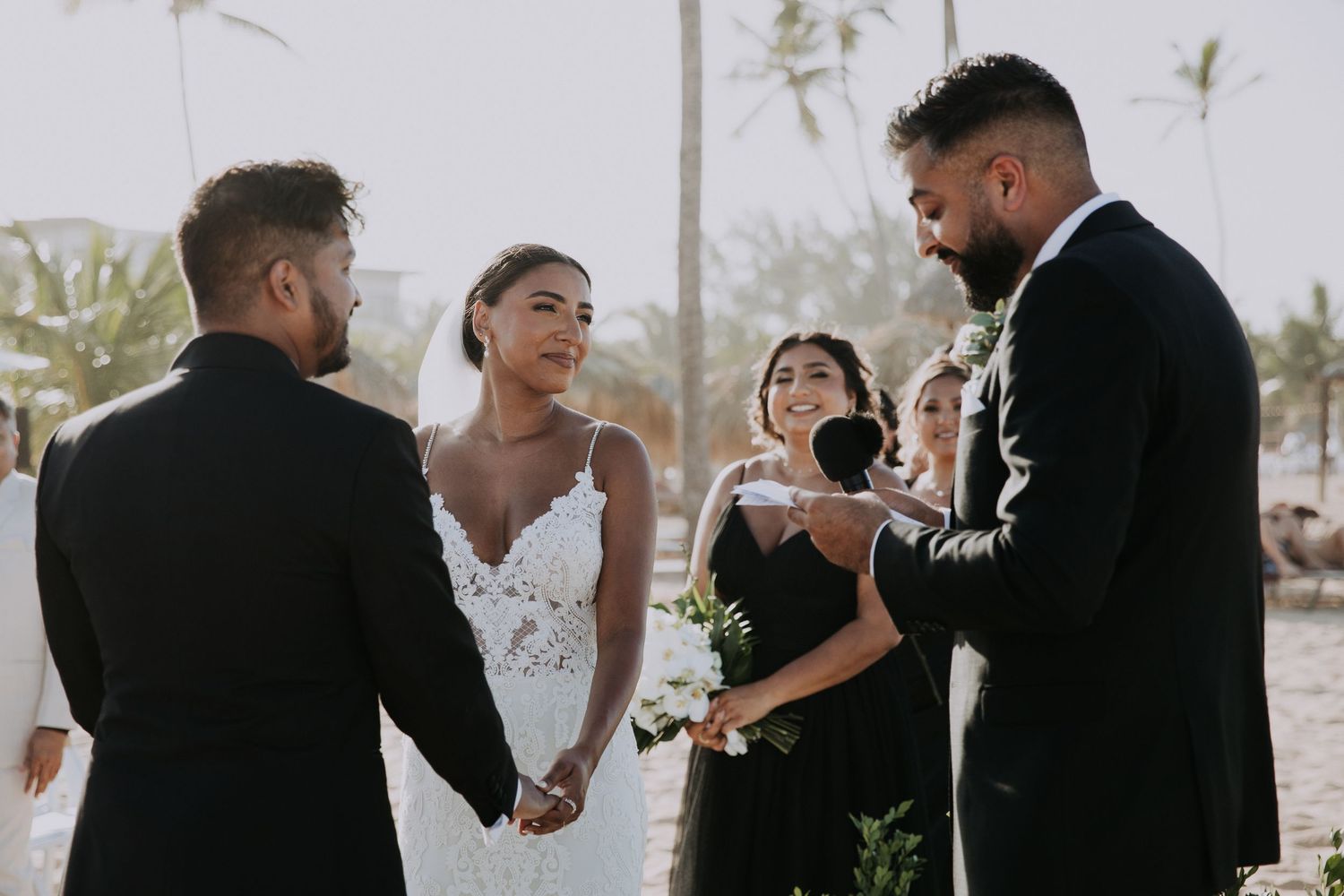 Wedding party shares joyful moments during outdoor beach ceremony at sunset.