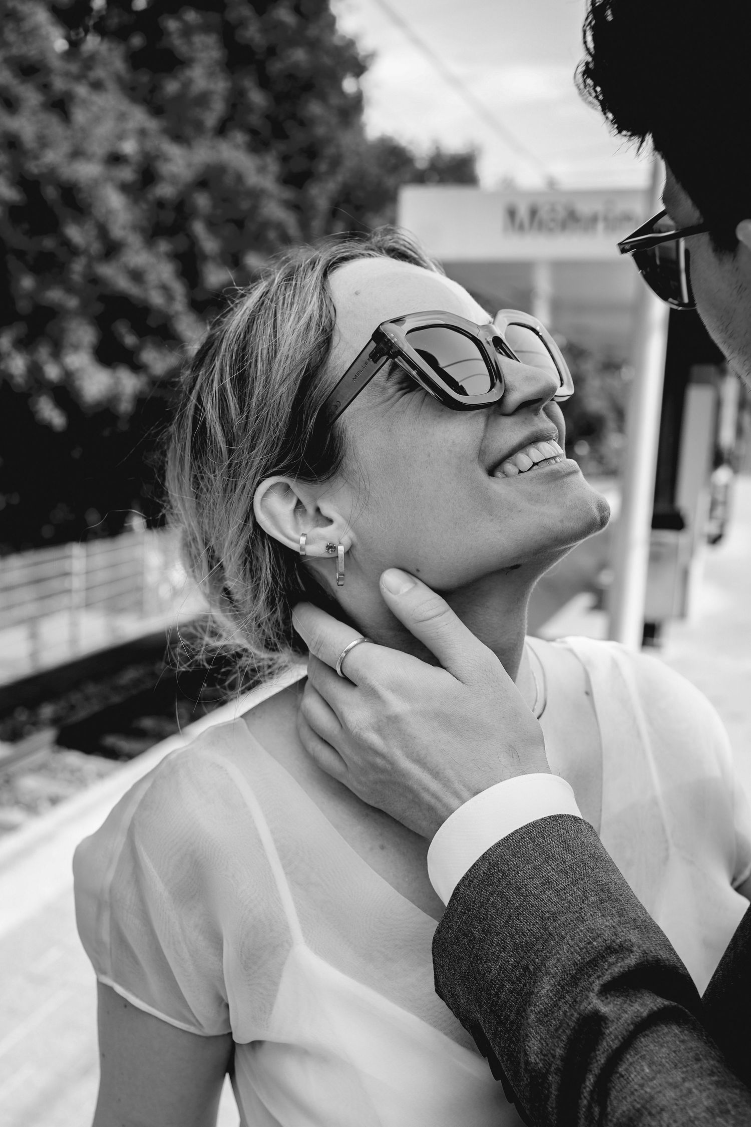 Black and white candid moment showing joyful laughter while wearing sunglasses and white shirt on a sunny day.