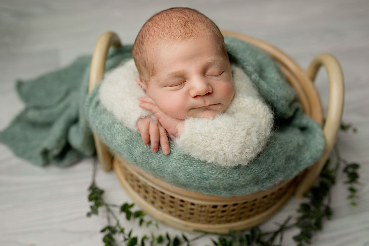 A sleeping newborn in a soft cream sweater lies in a curved fabric sling supported by hands against a blue backdrop. neutral colours, spring