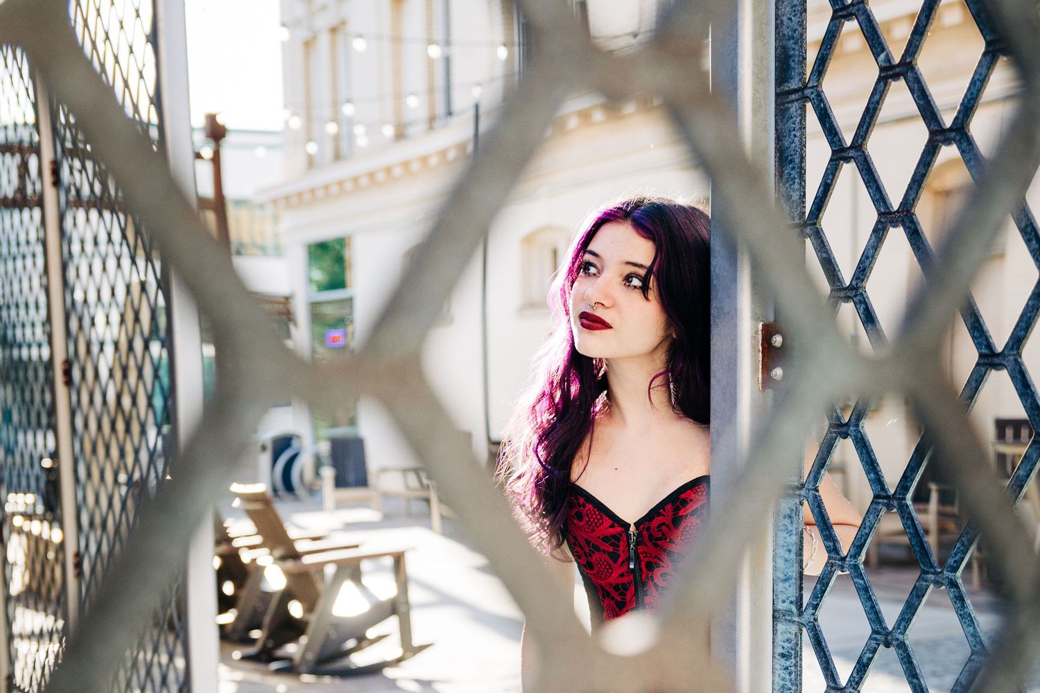 Creative portrait through a lattice fence showing pink hair and red clothing framed by geometric metal patterns.