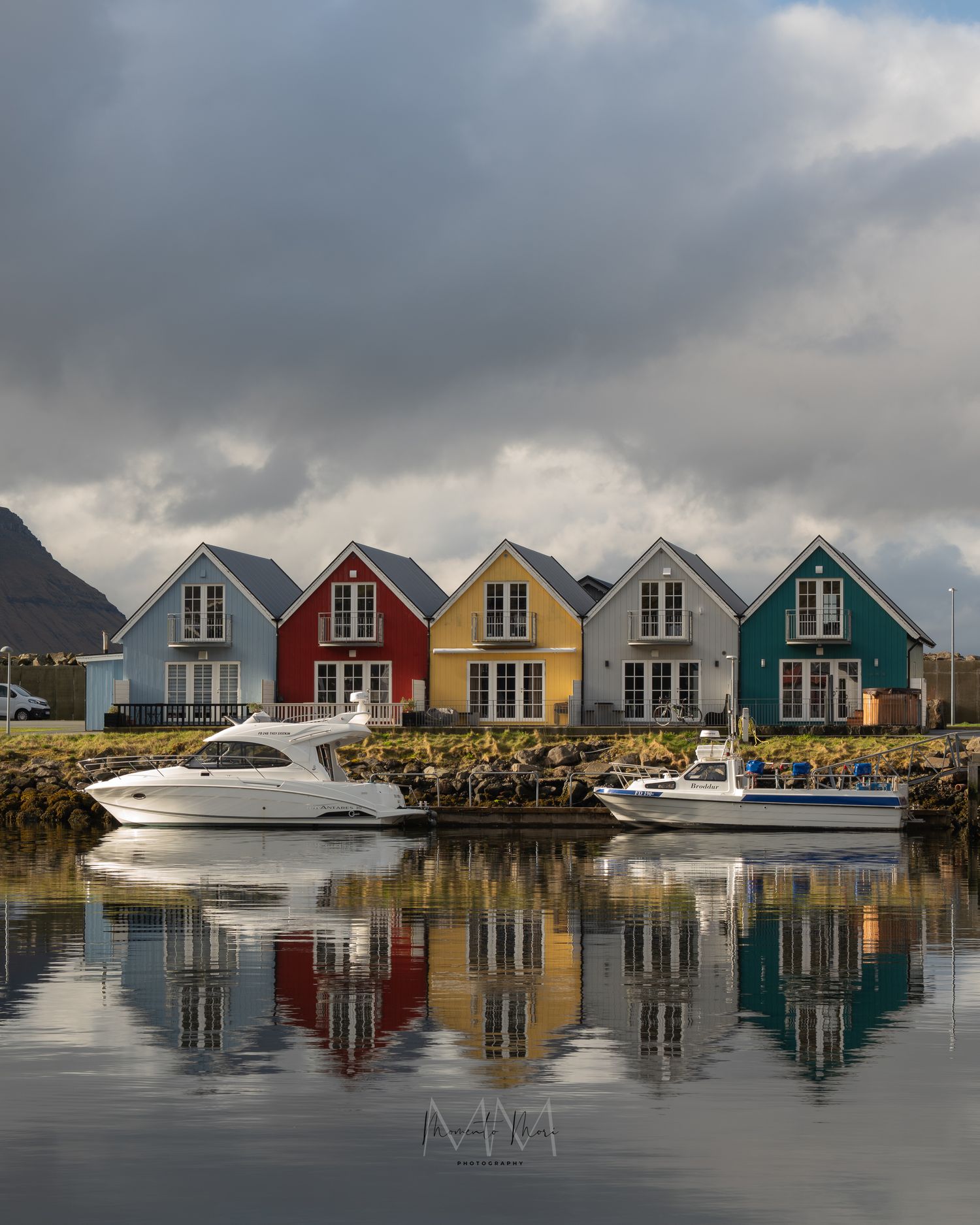 5 colorful cottages are reflected back by the water of a small harbor in front of them.