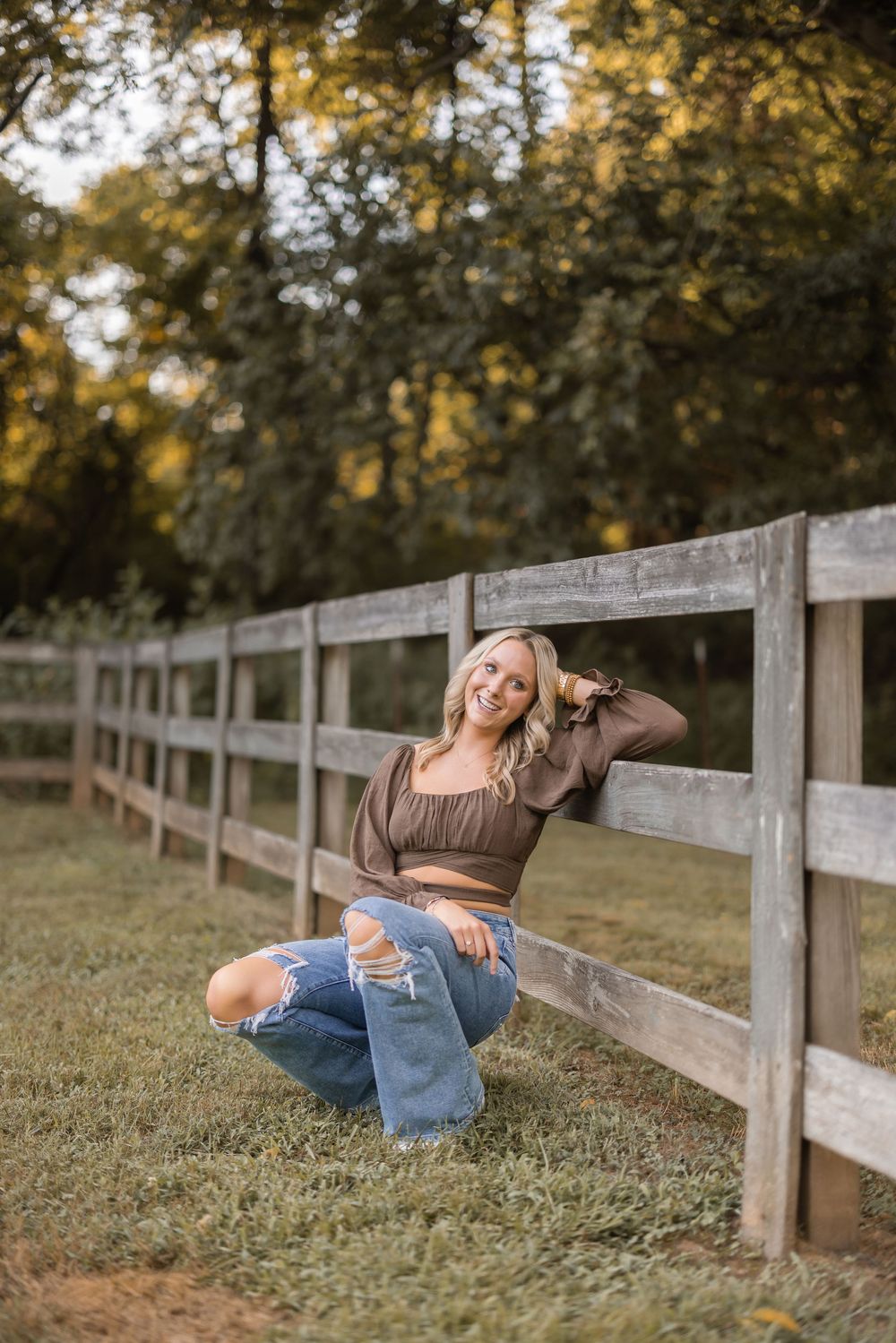 A casual lifestyle photo showing someone resting along a rustic wooden fence in a grassy field on a sunny day.