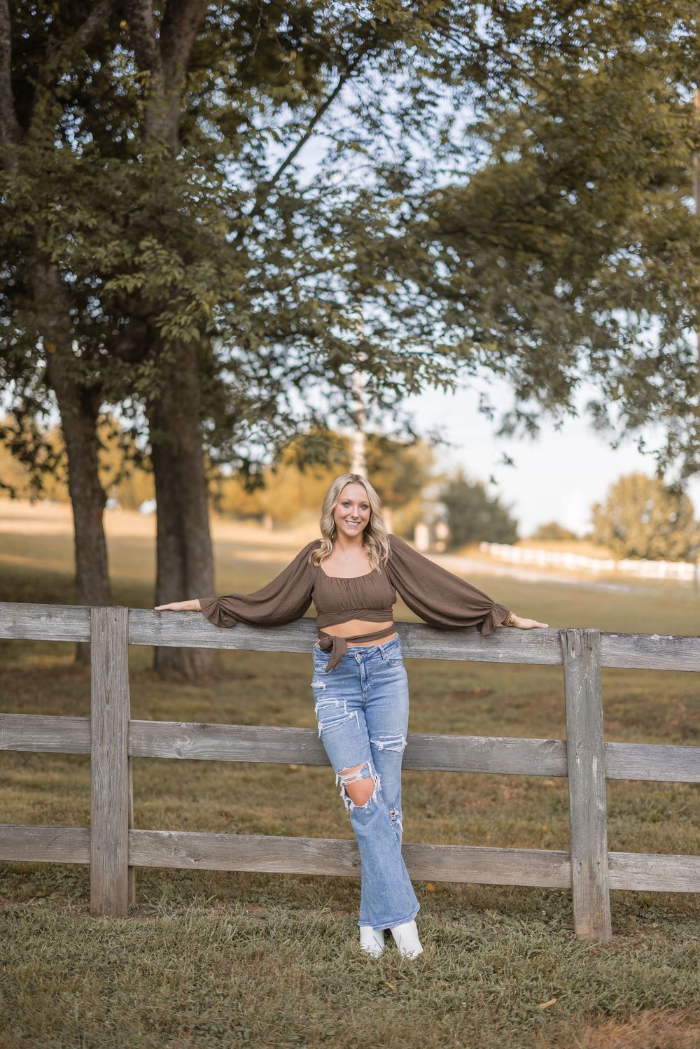 Casual portrait against a rustic wooden fence with trees and golden sunlight during sunset.
