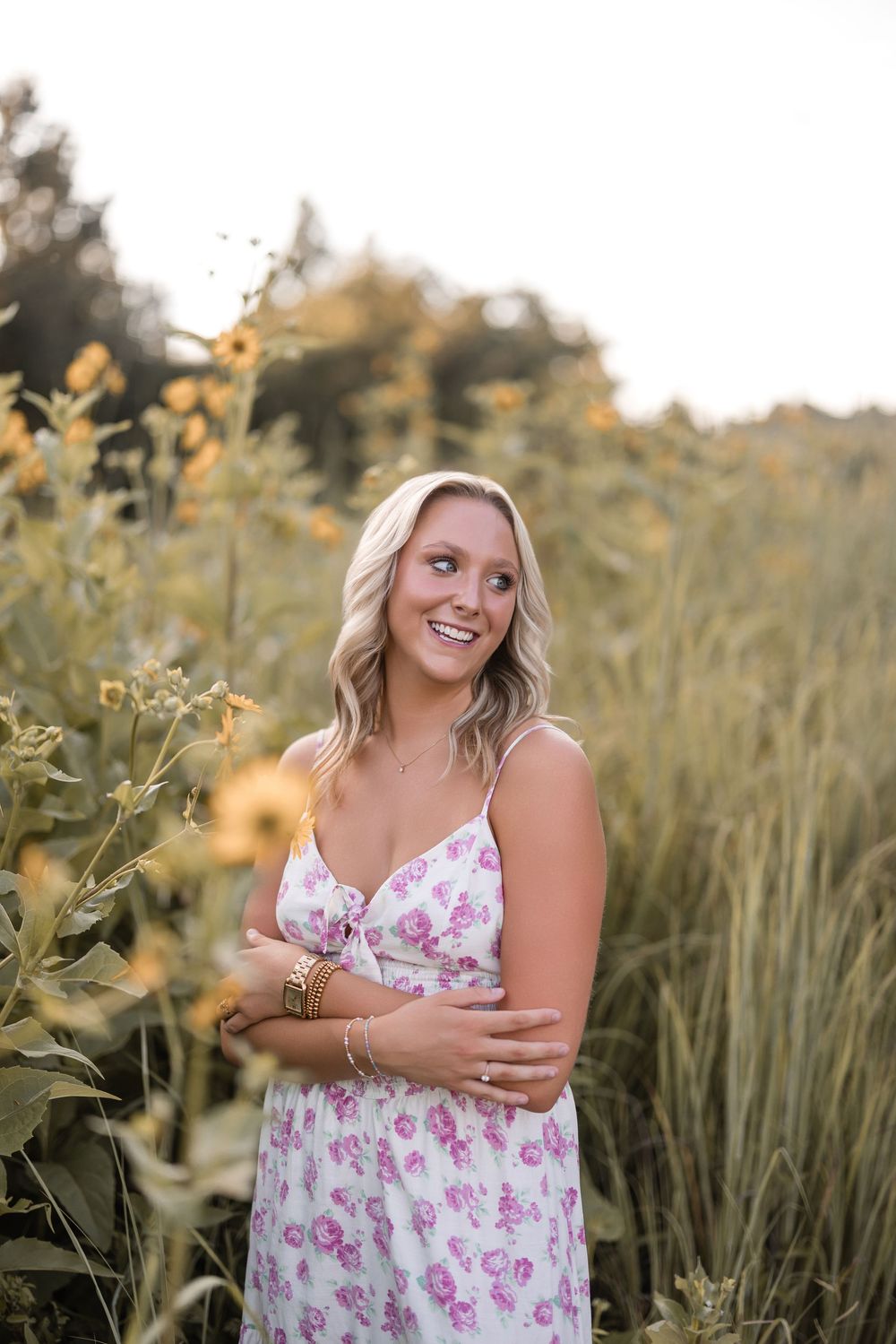 Portrait of someone standing in a floral dress among tall grasses and wildflowers during golden hour.